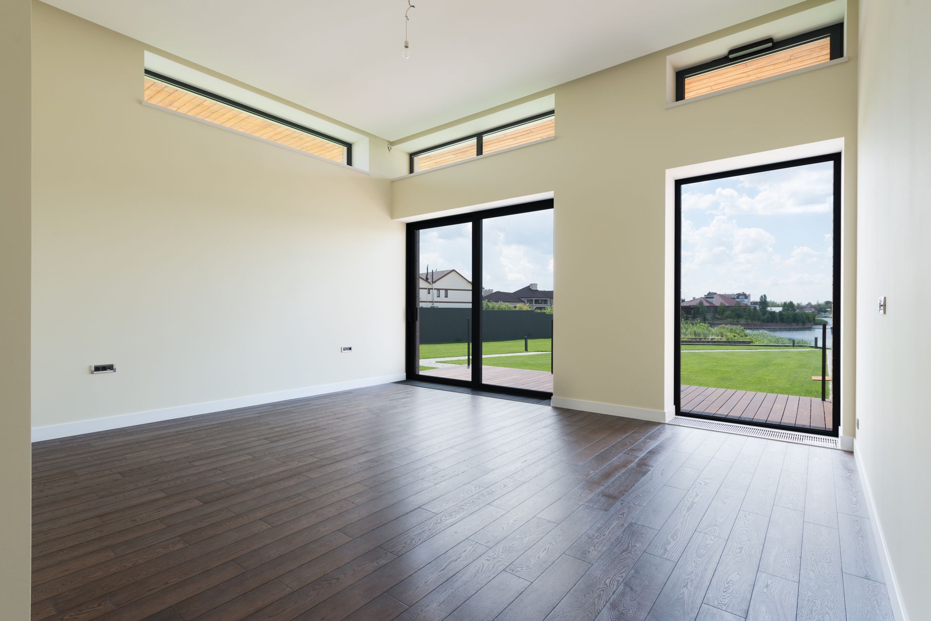 Salón luminoso con suelo de madera y grandes ventanales que se abren a una terraza y un jardín verde, instalado por Viktoria Ventanas.